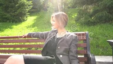 相机远离美丽的时尚年轻女子坐在阳光下的夏日公园的长凳上